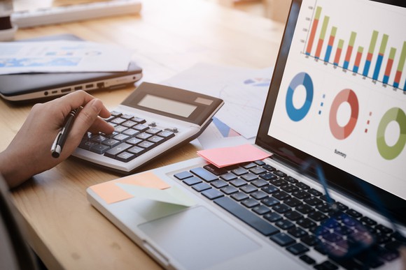 A hand on a calculator as someone does financial analysis at their desk.