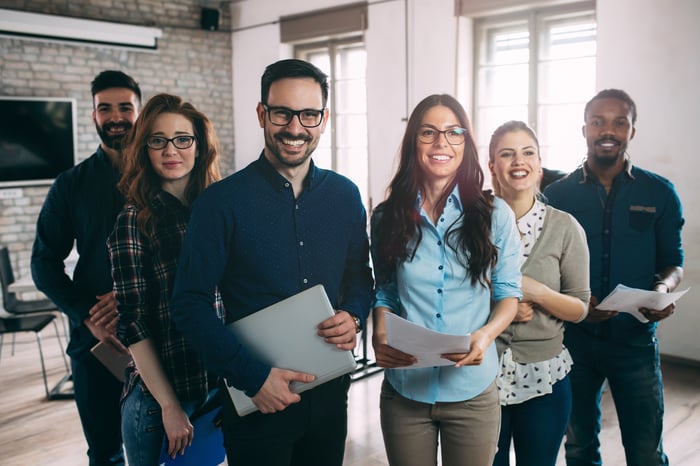 Group of young professional adults standing together while holding papers and smiling