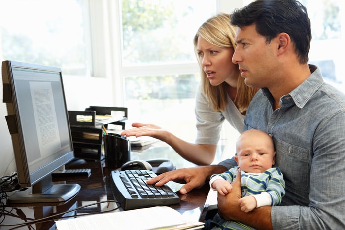 Worried parents holding a baby and reading an online article.