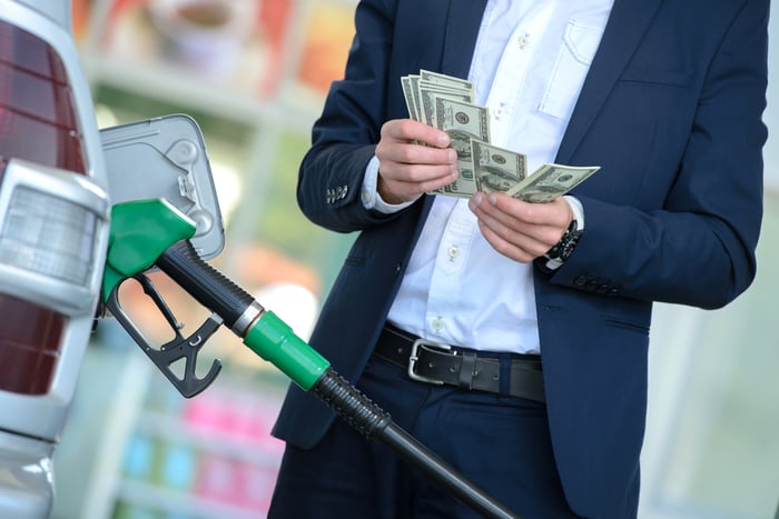 A person in a suit counting money while filling up a gas tank.