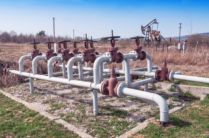 Natural gas pipelines and valves with an oil pump in the background.