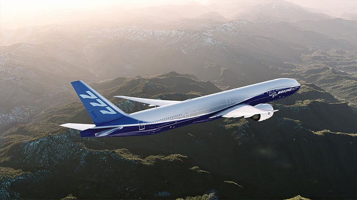 A Boeing 777-300ER flying over mountainous terrain