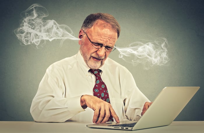 Steam is coming out of the ears of a man in a shirt and tie as he looks at his computer screen.