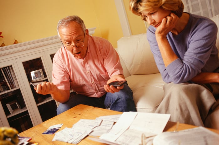 an older couple, looking sad and shocked at some papers in front of them