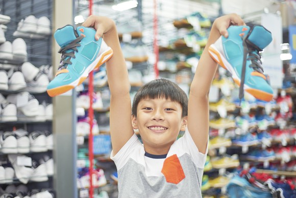 A young boy holds up a pair of sneakers.