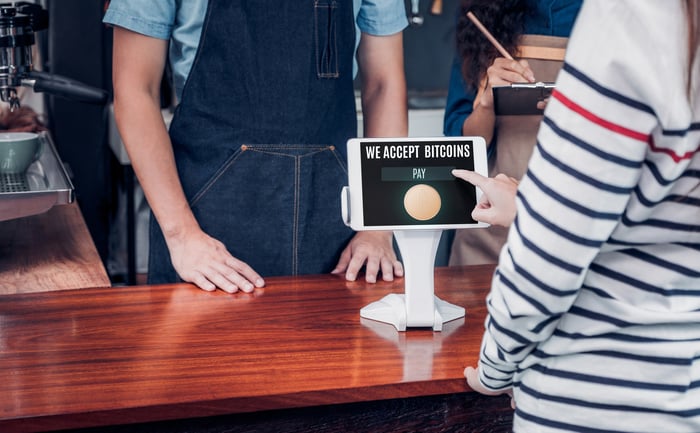 A woman using a point-of-sale device in a retail store to pay with bitcoin.