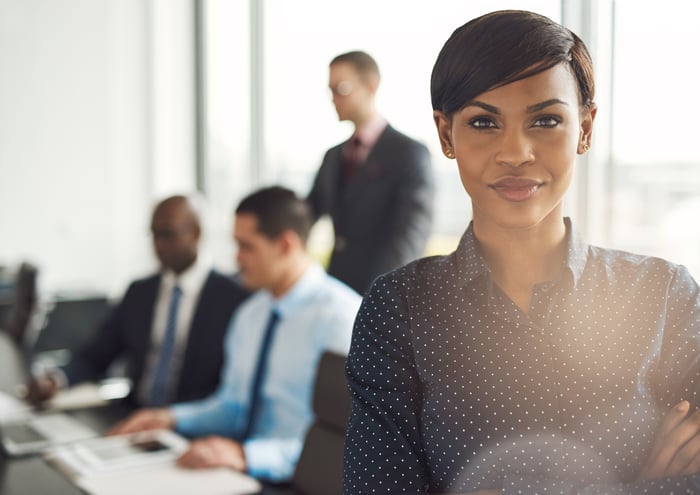 Woman leader in boardroom with men sitting at table.