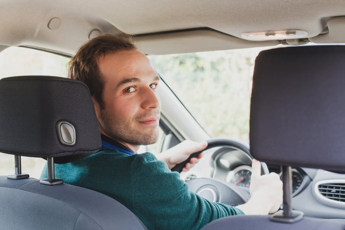 Man at the wheel of a car, looking back over his shoulder, presumably at a passenger