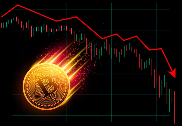 A physical gold bitcoin on fire and heading lower with a declining chart in the background.