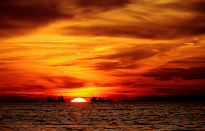 Tanker ships out on the water with an orange sunset in the background.