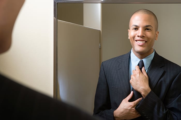 Man in suit adjusting tie in the mirror.