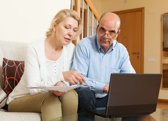 A mature couple going over the finances on a laptop, with the husband clearly irritated.