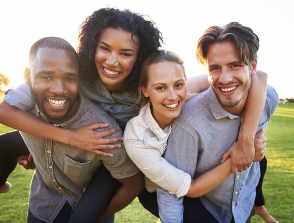 Four young adults, two men and two women, smile arm in arm outdoors.