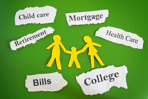 Paper cutouts of a family, and torn pieces of paper bearing words such as bills, college, mortgage, healthcare, etc.