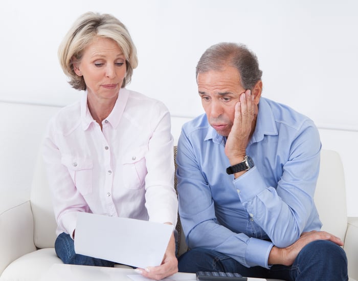 A worried senior couple review a document as they sit side by side.