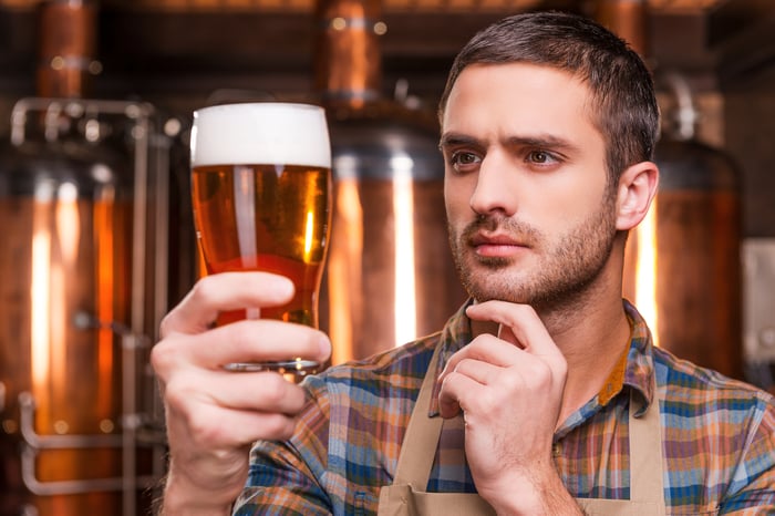 A brewer closely examining a pint of beer being held in his hand.