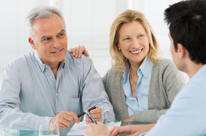 A senior couple talking to a younger man over a table.