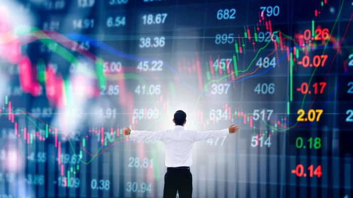 Man with outstretched arms in front of giant stock information screen