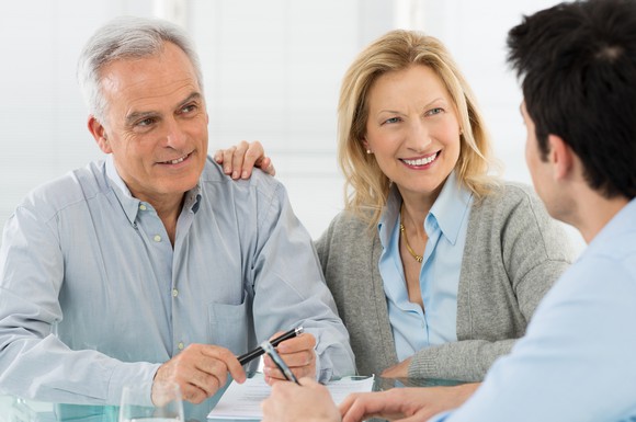 An older couple talking to a younger man over a table.