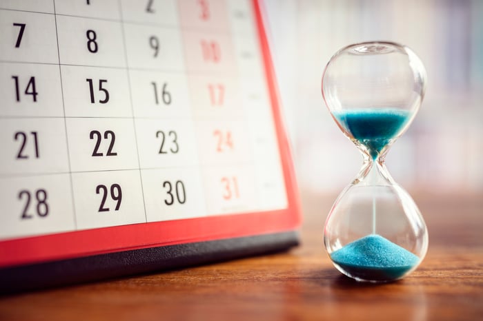 An hourglass next to a calendar on a table. 