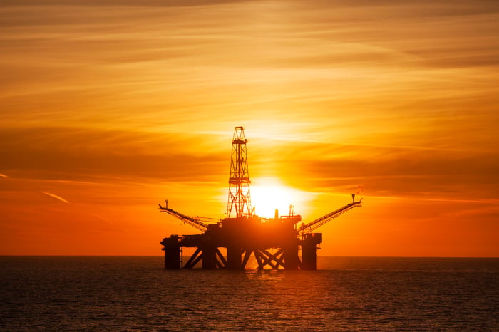 An offshore driling rig with the sun setting in the background.