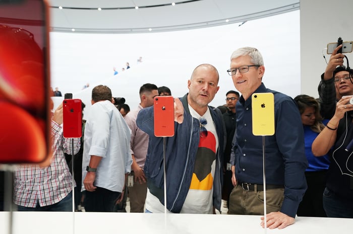 Apple executives Jony Ive and Tim Cook at a table with iPhone XR phones.