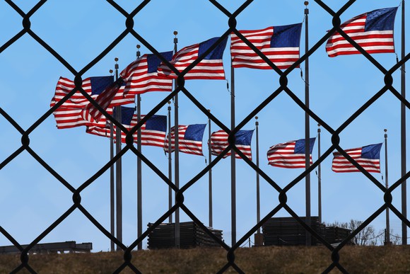 View through a chain-link fence at U.S. flags
