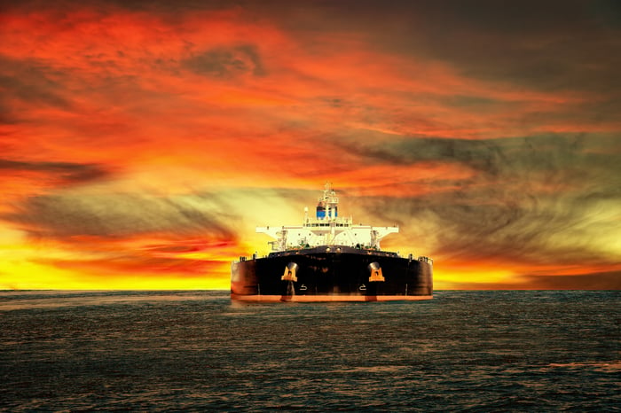 An oil tanker with a bright red and yellow sky in the background.