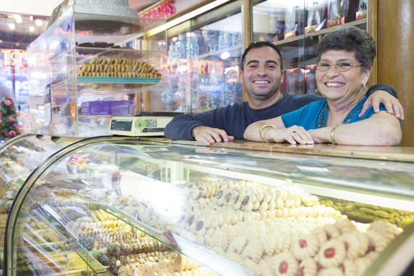 A youmger man has his arm around an older woman at the counter of a bakery.