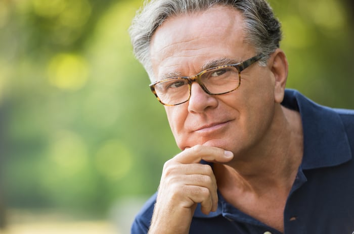 A bespectacled baby boomer in deep thought with his hand on his chin. 