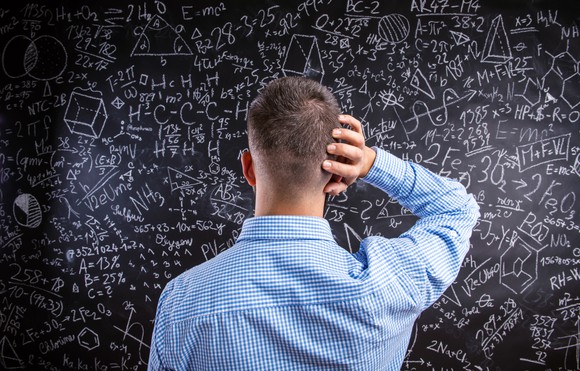 Confused man staring at blackboard with calculations.
