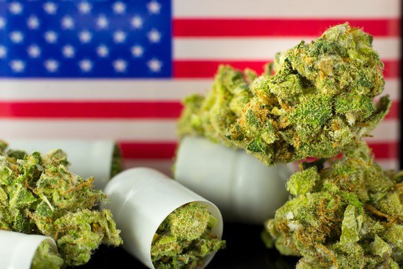 Marijuana buds spill out of bottles in front of a U.S. flag.