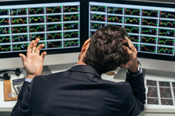 A frustrated investor with his hand on the top of his head while looking at stock charts on his computer monitors.