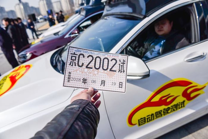 A hand holding a permit in front of a car and driver.