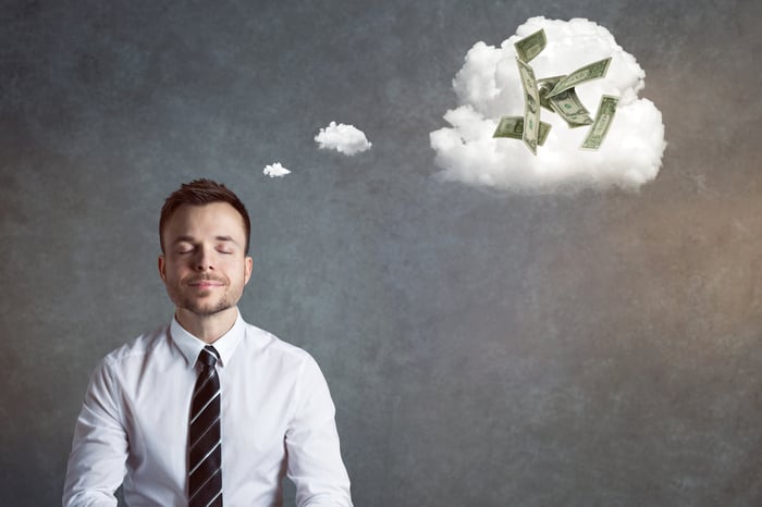 A man in a shirt and tie with a dream cloud above his head containing $1 bills.