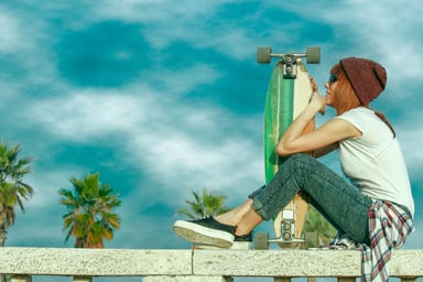 Skater girl sitting on a railing holding her board