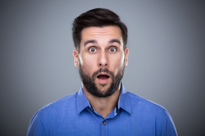 A bearded man wearing a blue shirt and looking surprised