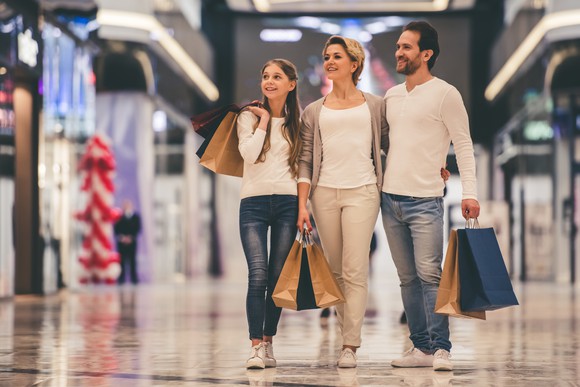 Family of three walking through a mall while carrying shopping bags.