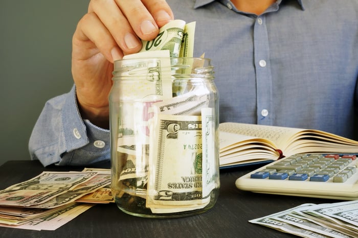 Man putting a 20-dollar bill into a jar of cash