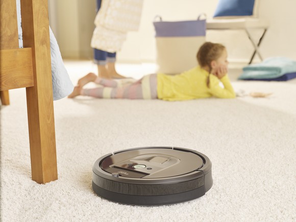 iRobot Roomba 980 cleaning carpet in a home, while a child lies on the floor nearby.