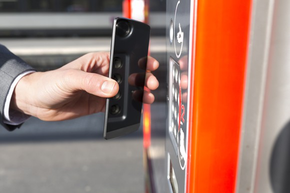 Man using mobile phone to make a contactless payment at machine on train platform.