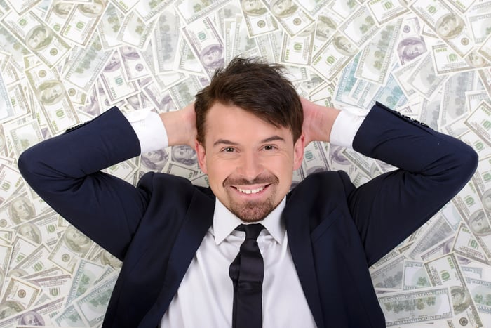 A wealthy businessman in a suit lying atop a messy pile of cash. 