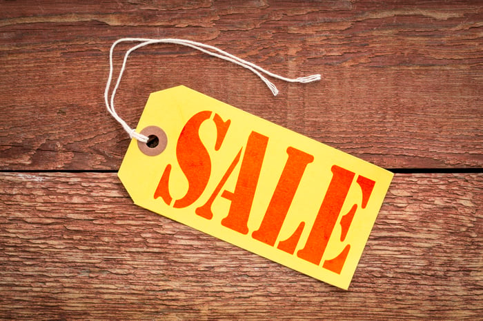 A sale sign on a yellow paper price tag against rustic wood.