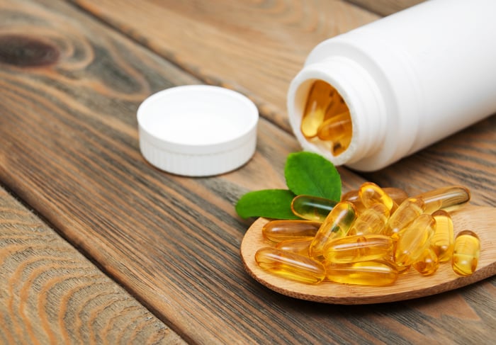 A tipped over white bottle filled with softgel capsules, as well as a small pile of capsules lying next to the bottle.