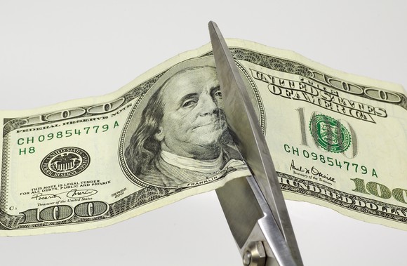 Scissors cutting $100 bill in half.