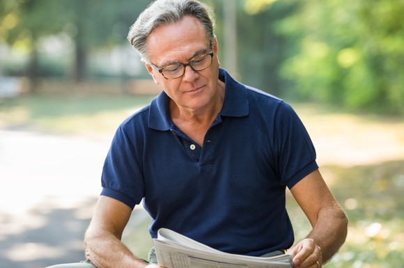 Older man reading newspaper outdoors.