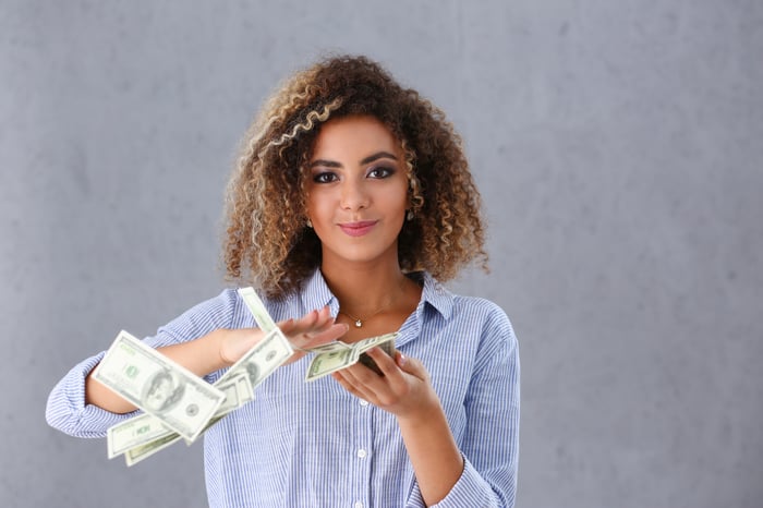 A young woman sweeps hundred dollar bills off her outstretched hand.