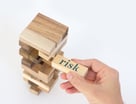 GETTY IMAGES A hand pulls a wooden Jenga block labeled 'risk' from a precariously balanced Jenga tower