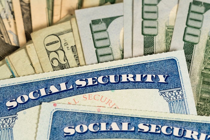 Two Social Security cards lying atop fanned piles of cash bills.