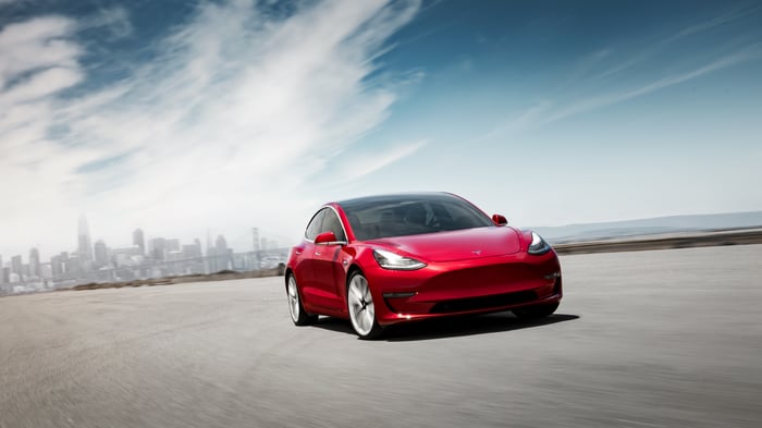 A red Tesla Model 3 with a city skyline in the background